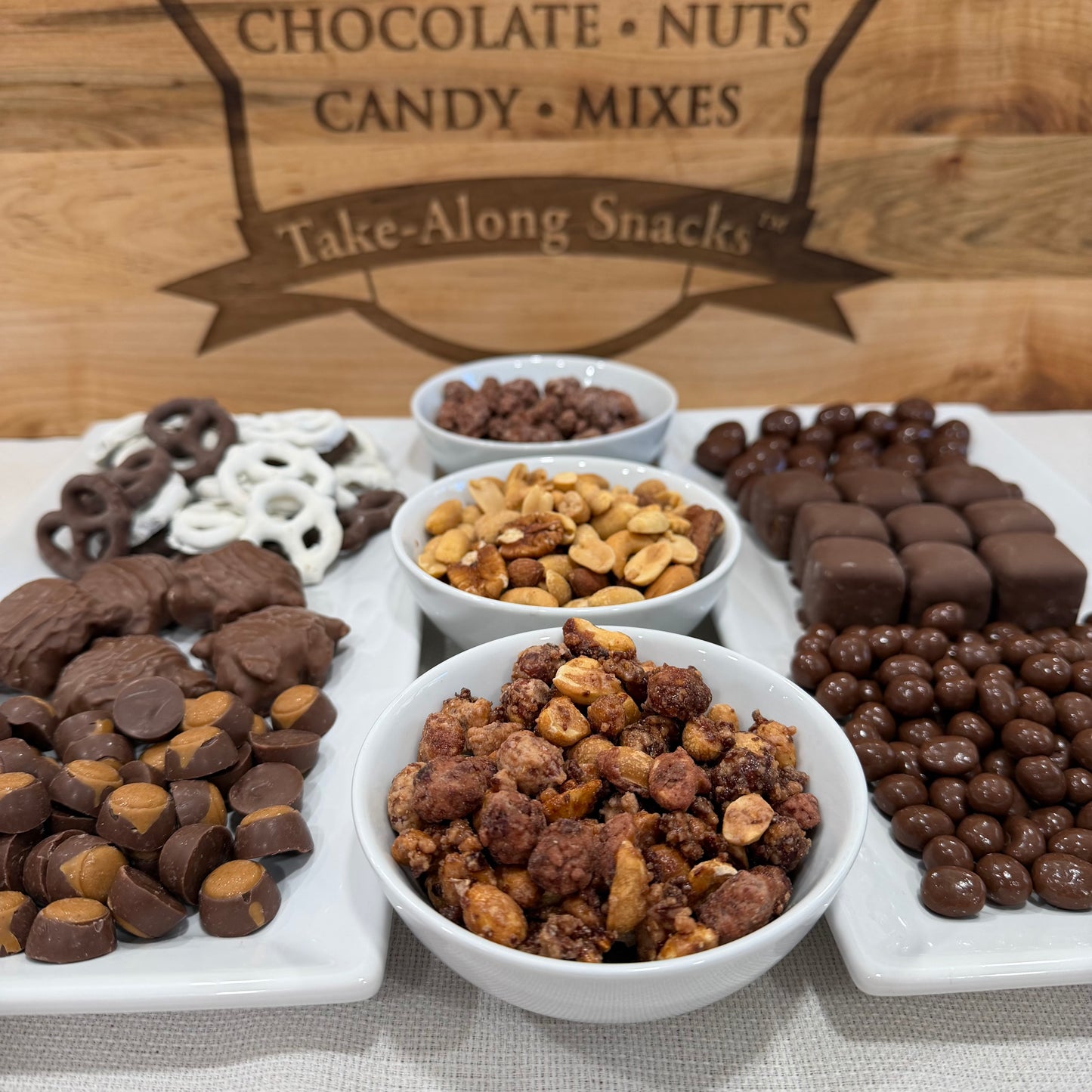 Assorted chocolate, nuts, and candy mixes on a platter with a wooden background.
