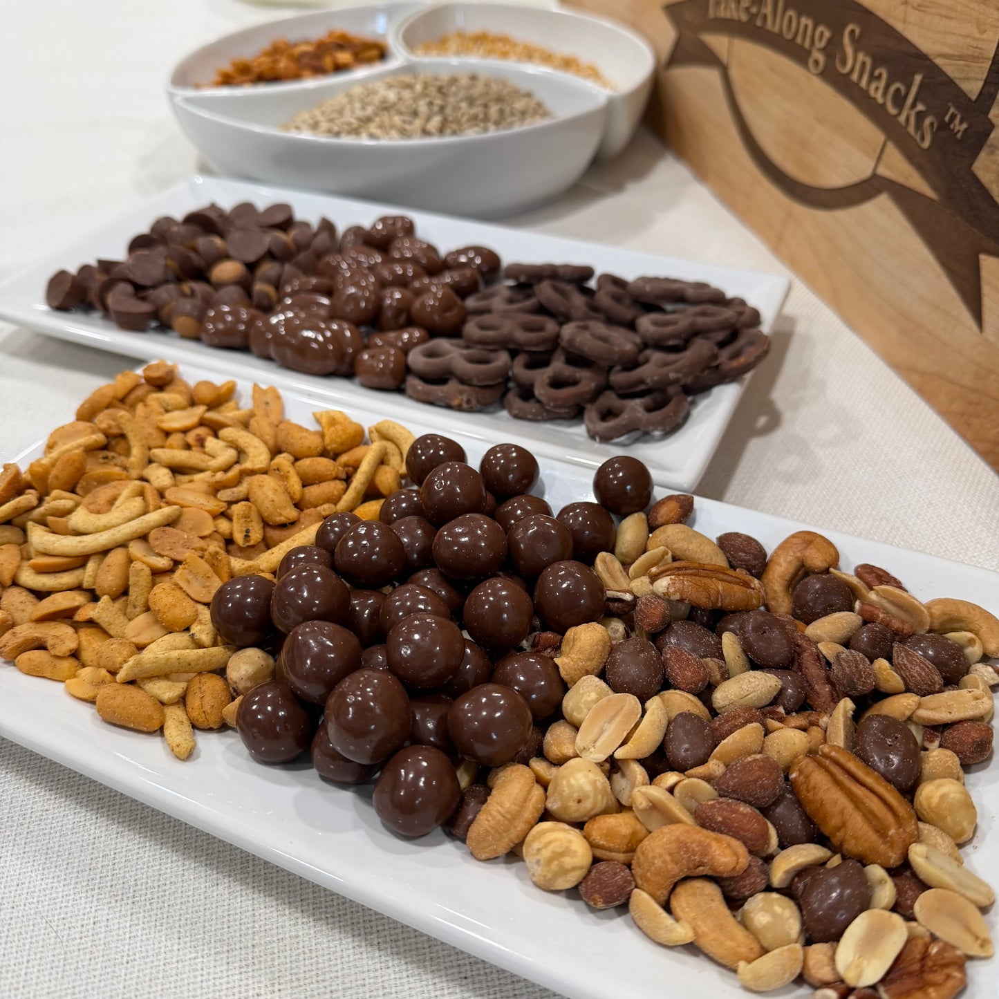 Assorted snacks including chocolate-covered pretzels, nuts, and dried fruits on a white tray.