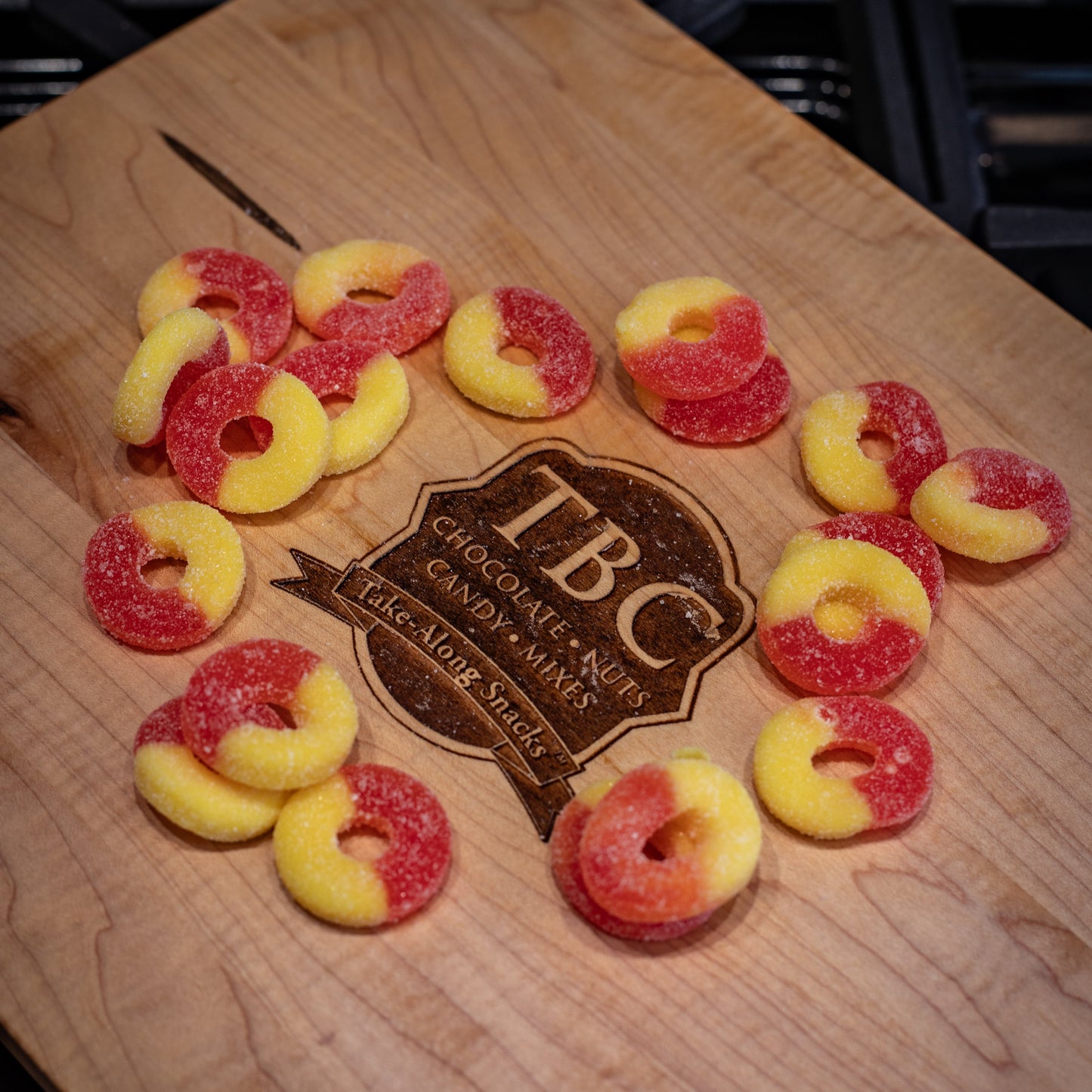 Gummy candy rings on a wooden board with TBC Gourmet Candy Co. branding.