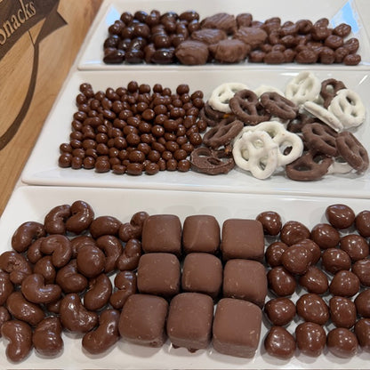 Assorted chocolate-covered snacks including nuts, pretzels, and candy on a white tray.