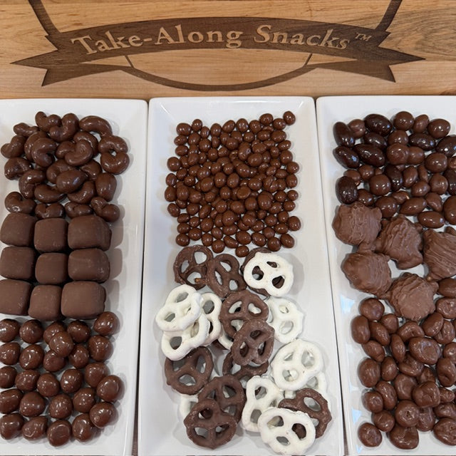 Assorted chocolate-covered snacks on a wooden board with 'Take-Along Snacks' branding.
