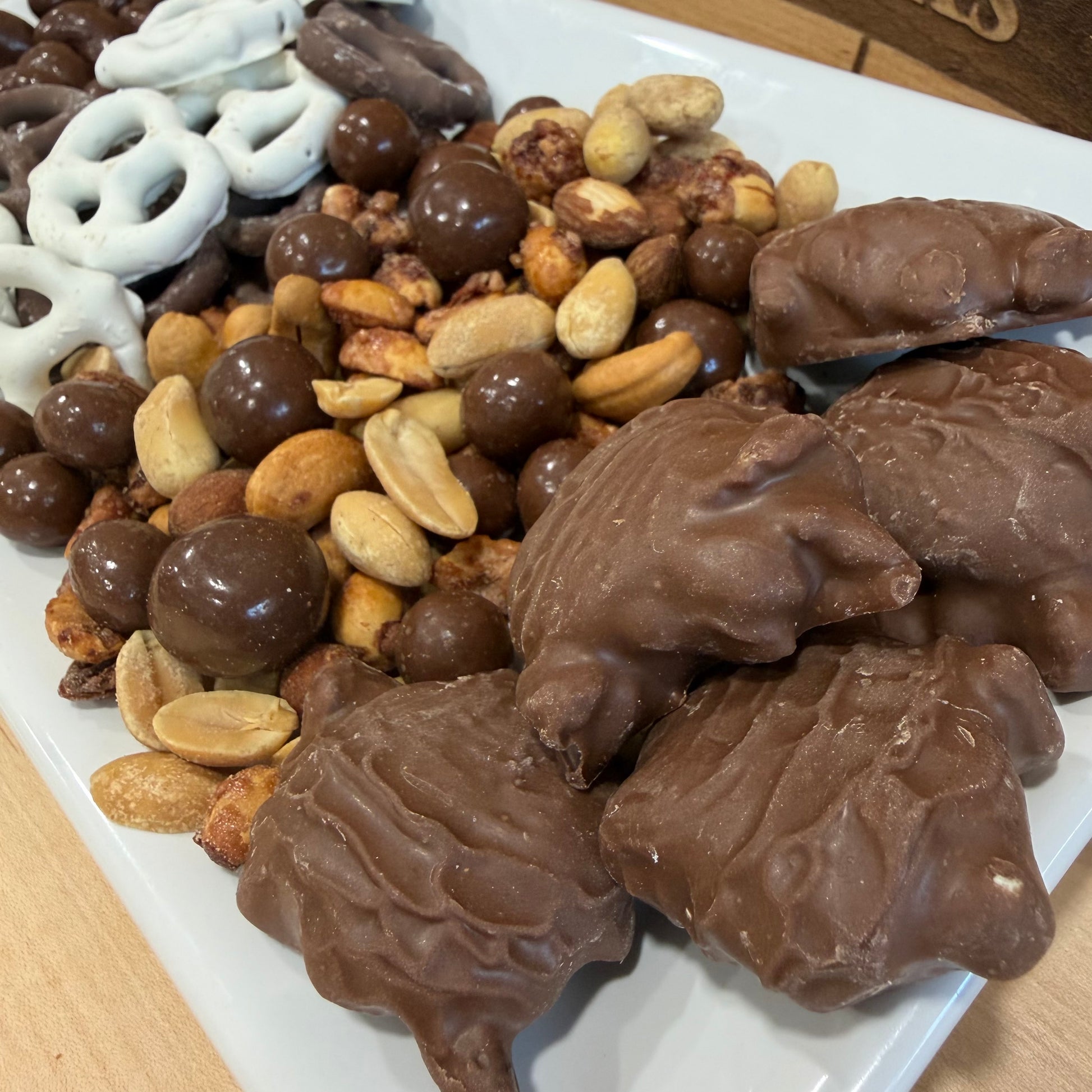 Assorted chocolate-covered treats including nuts and pretzels on a white plate.