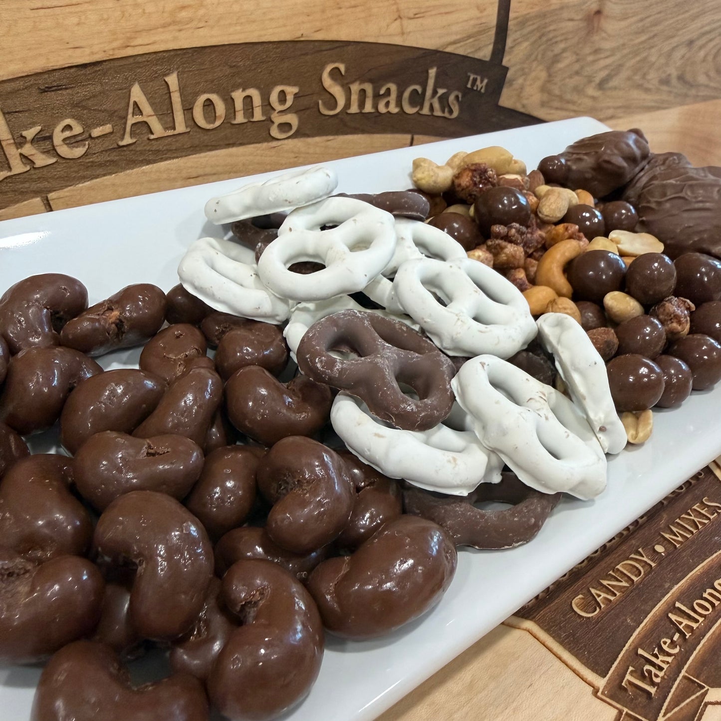 Assorted chocolate-covered snacks on a platter with 'Tate-Along Snacks' branding.
