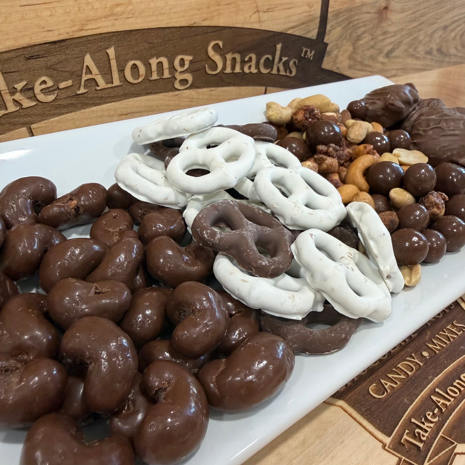 Assorted chocolate-covered snacks on a platter with 'Tate-Along Snacks' branding.