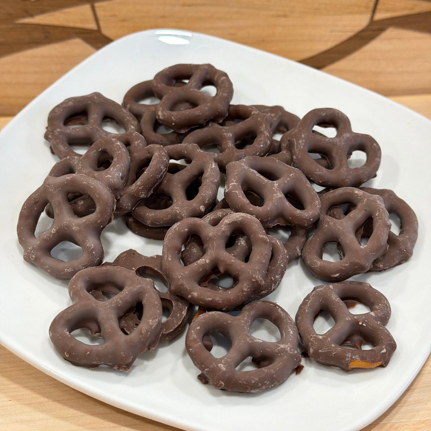 Chocolate-covered pretzels on a white plate with a wooden background