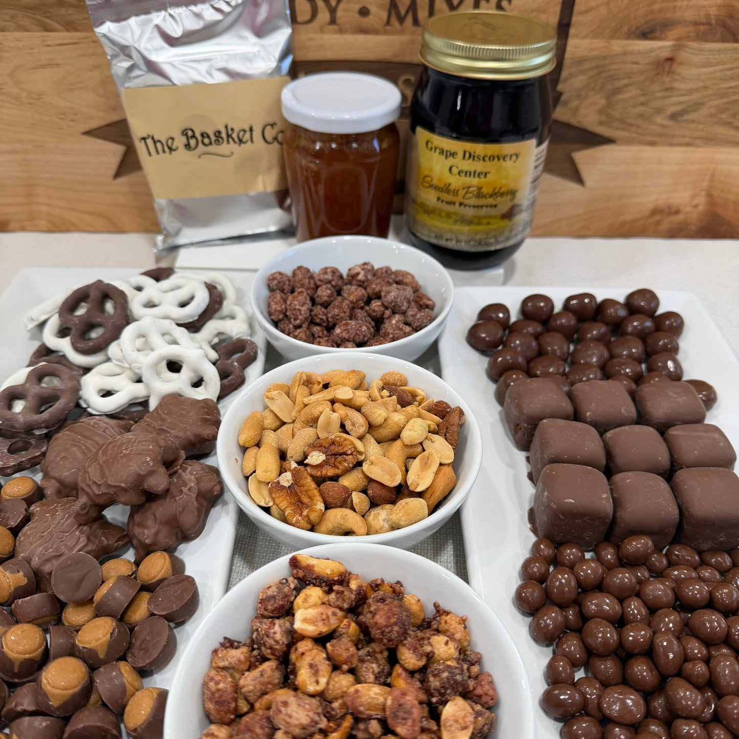 Assorted chocolate-covered treats and nuts on a wooden board with a 'Chocolate Nuts' sign.