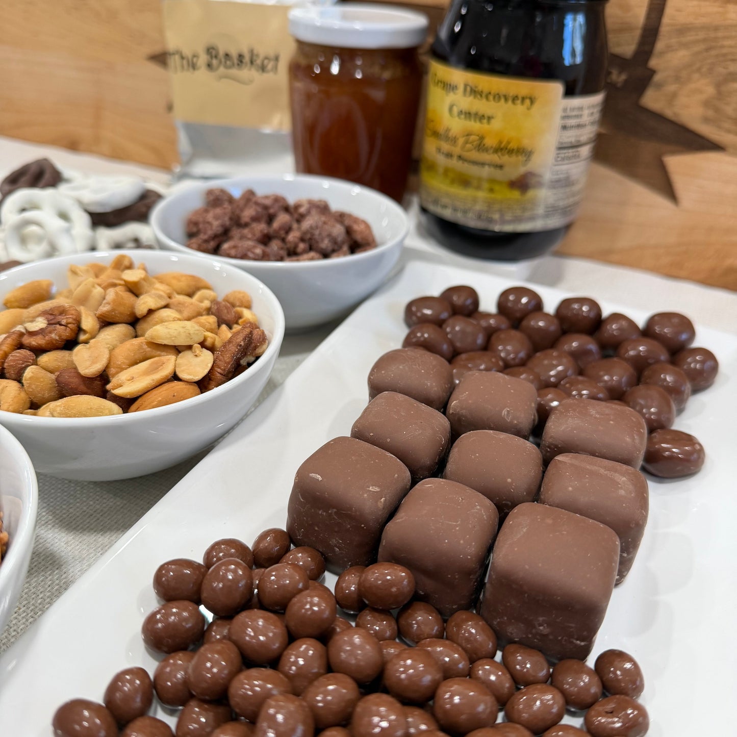 Assorted chocolate-covered treats and nuts on a white plate with a wooden background.
