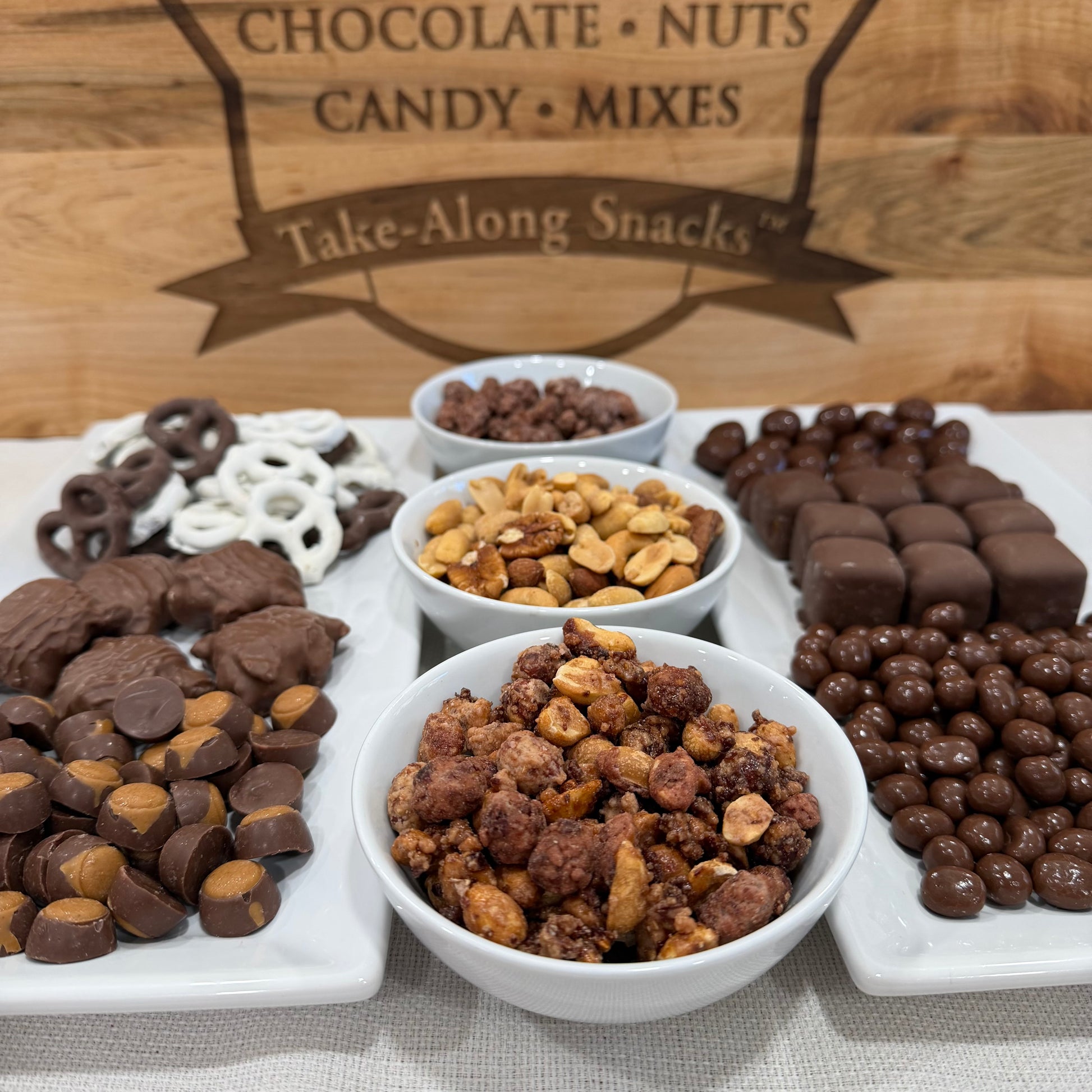 Assorted chocolate, nuts, and candy mixes on a platter with a wooden background.