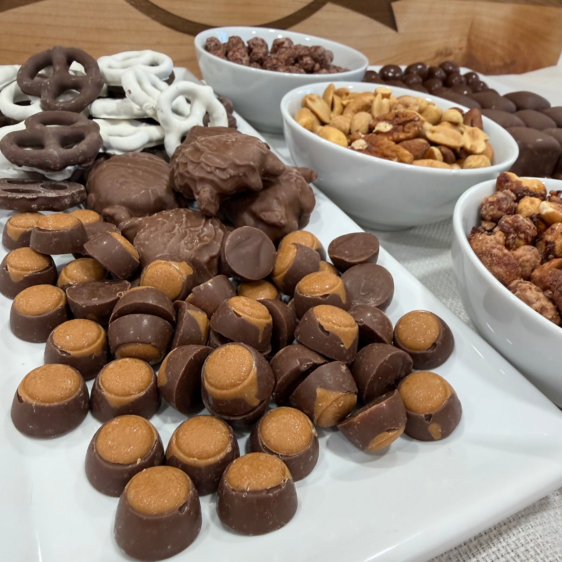 Assorted chocolate candies and nuts on a white plate with bowls of more snacks in the background.