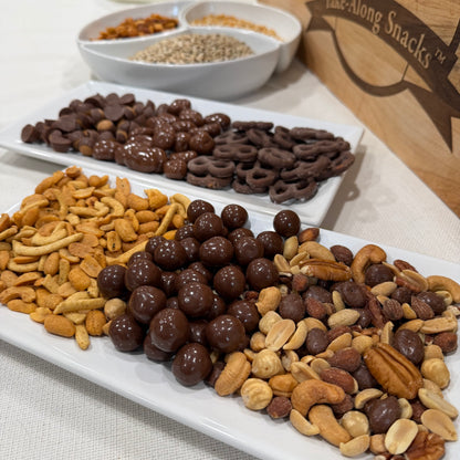 Assorted snacks including chocolate-covered pretzels, nuts, and dried fruits on a white tray.