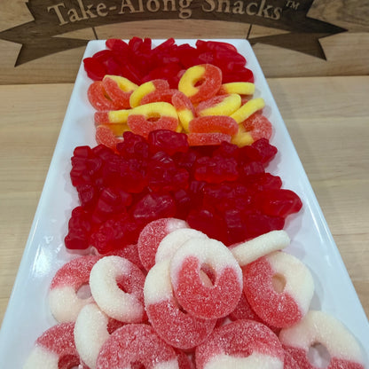 Assorted gummy candies including red, yellow, and white gummies on a white tray with 'Take-Along Snacks' branding.