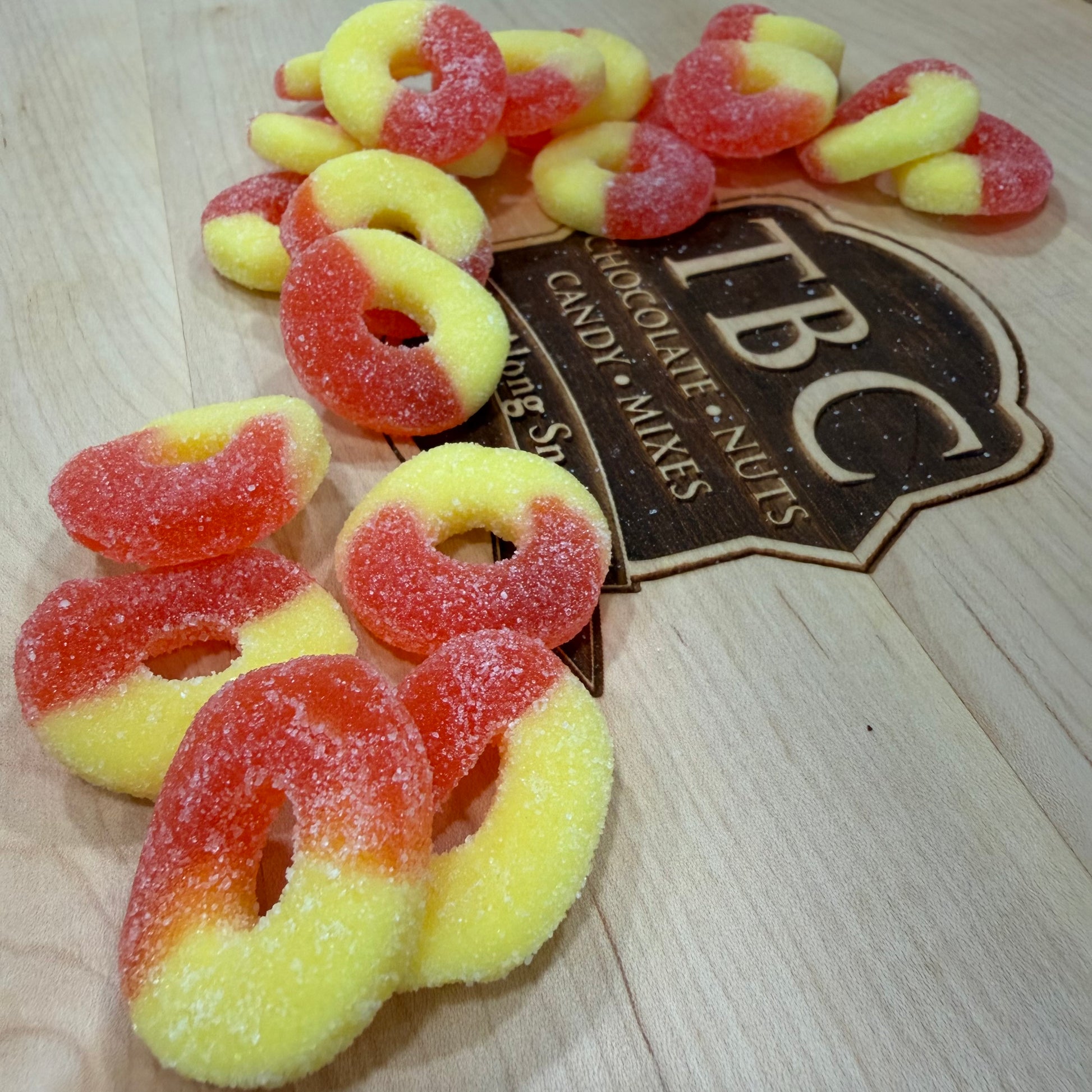 Colorful candy peach ring gummies on a wooden surface with TBC Candy Mixes branding.