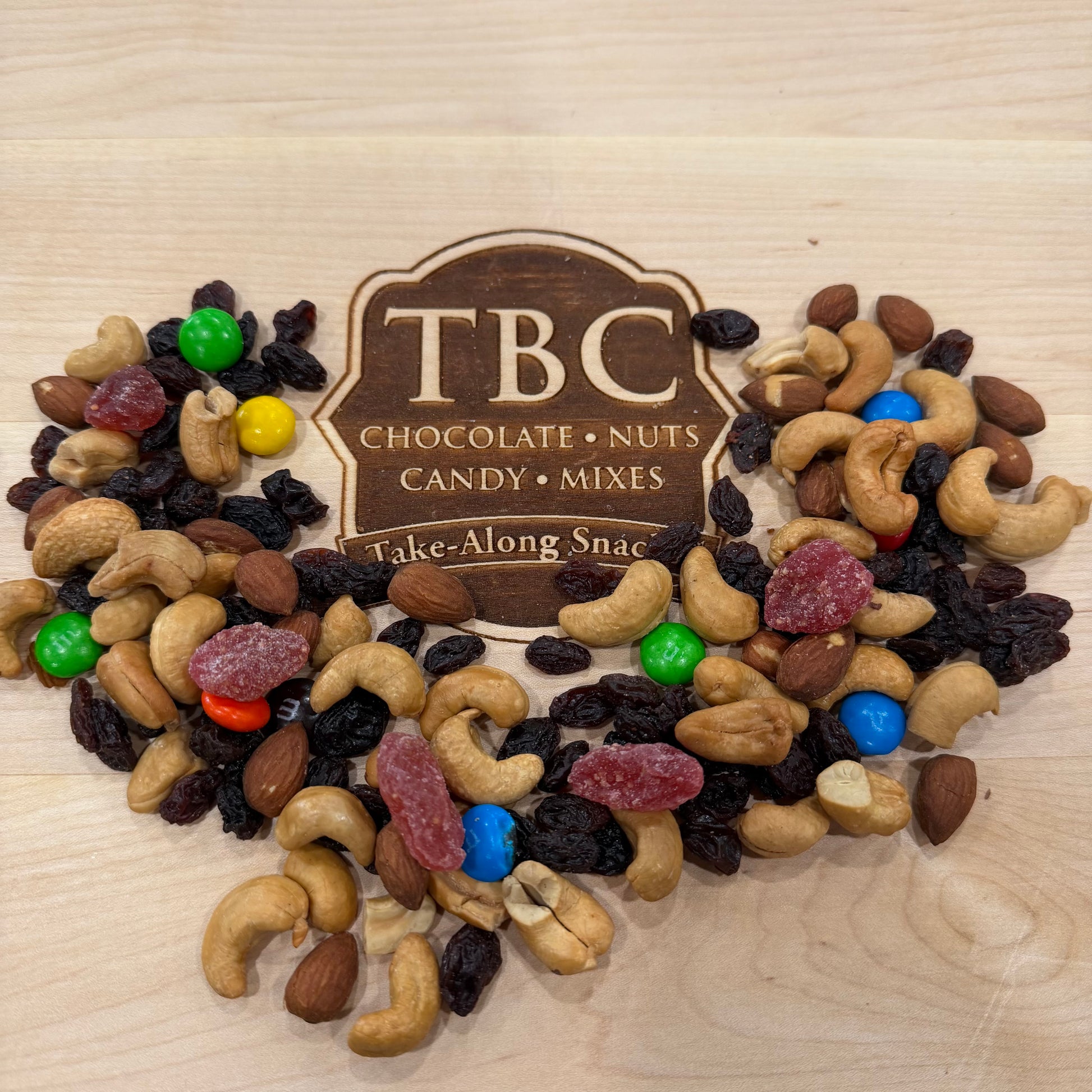 Assorted nuts and candy mix with TBC branding on a wooden surface
